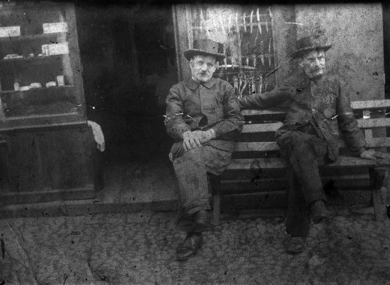 Deux hommes assis sur un banc devant une devanture (veirina) de coutelier (cotelièr), rue du Valat, vers 1885