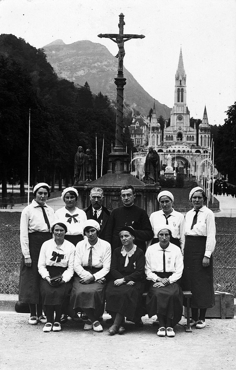 Paroissiens (parroquians) et curé (curat) devant calvaire (calvari) et basilique, à Lourdes (65), 1939