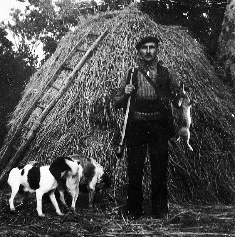 Chien et chasseur (caçaire) montrant un lapin devant une meule de paille (palhièr) circulaire, à Courti