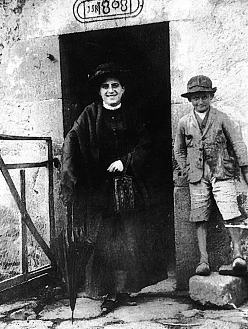 Femme costumée et jeune garçon sur un pas de porte, à Ladignac