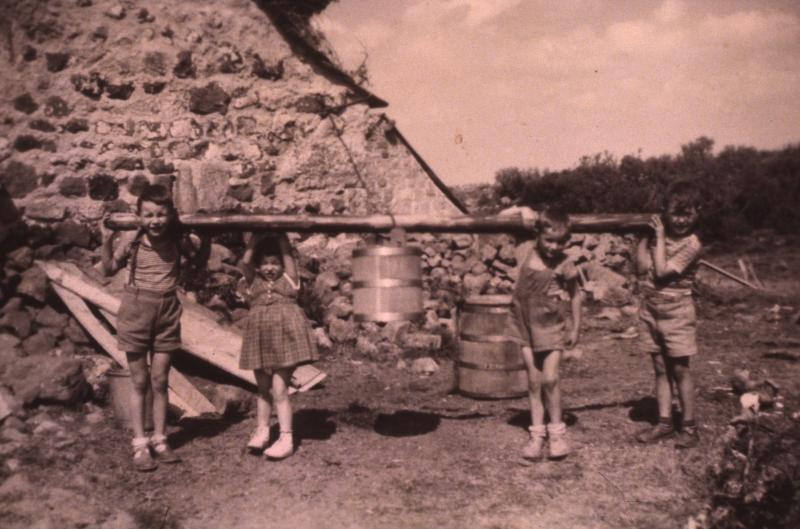 Transport à dos d'enfant d'un seau en bois (farrat) devant un buron (masuc), au Cher, commune de Nasbinals (48), 1954