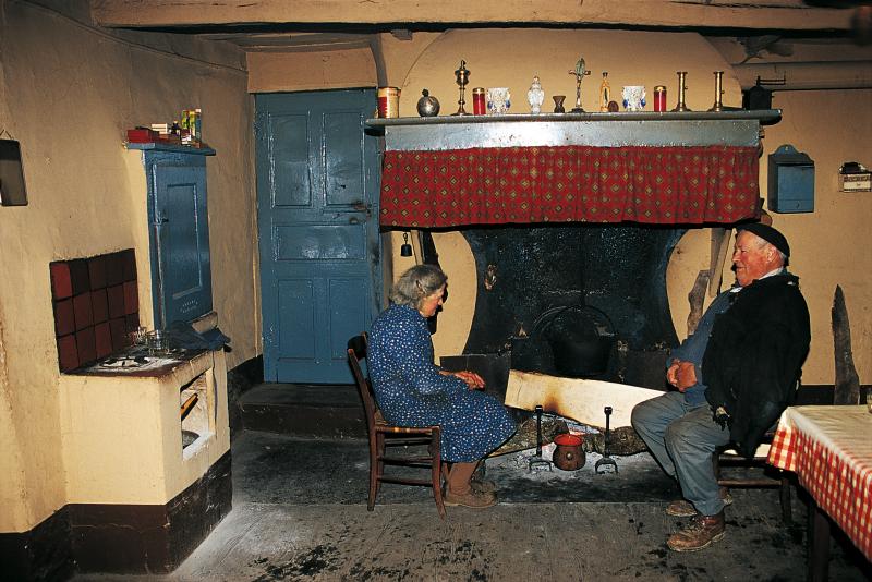 Foyer de cuisine (potatgièr), femme et homme se chauffant devant le feu (canton), à La Graverie, janvier 2000.