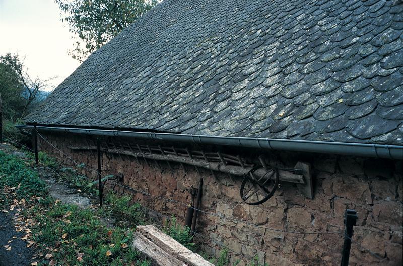 Rancher ou “échelle d'écureuil” (escarràs, escala d'esquiròl) remisé sous un avant-toit de grange, en Haute Vallée d'Olt (canton d'Estaing), octobre 1994