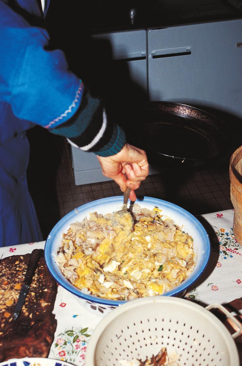 Main d'une femme remuant le stockfish (estafin, estòfin, estofinada) dans un plat en émail, à Cantagrel, juin 2000