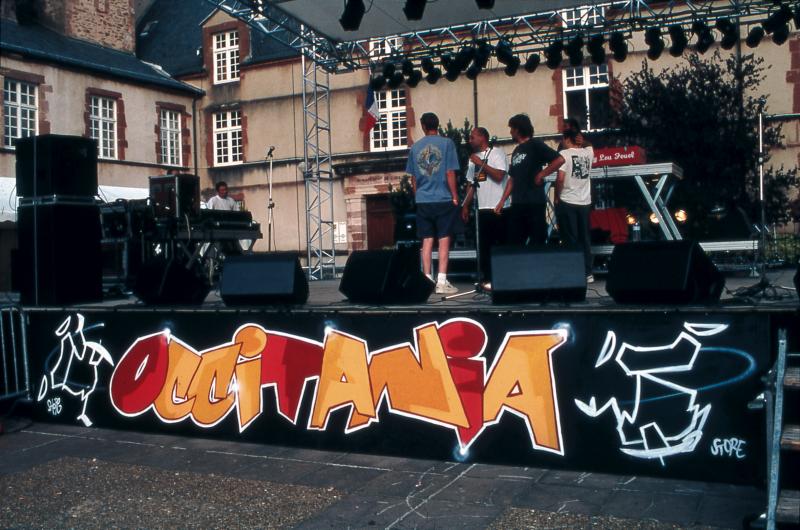 Panneau de devant d'estrade en occitan et techniciens sur scène dans le cadre de l'Estivada 1999