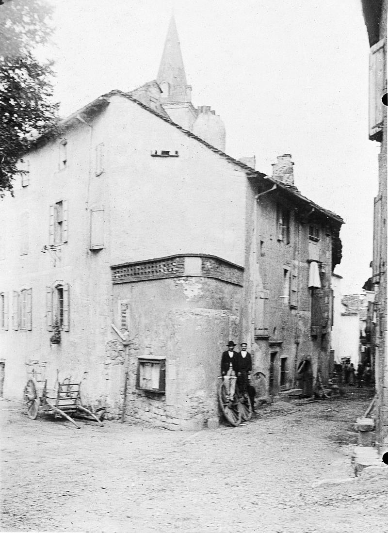 Char (carri), placard d'affichage et deux hommes juchés sur des roues (ròdas) de char devant une maison (ostal)