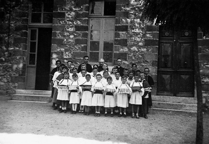 ​Enfants de chœur (clergues) en aubes avec petites corbeilles (desquets) et curés (curats) en soutane pour la Fête-Dieu, 1942