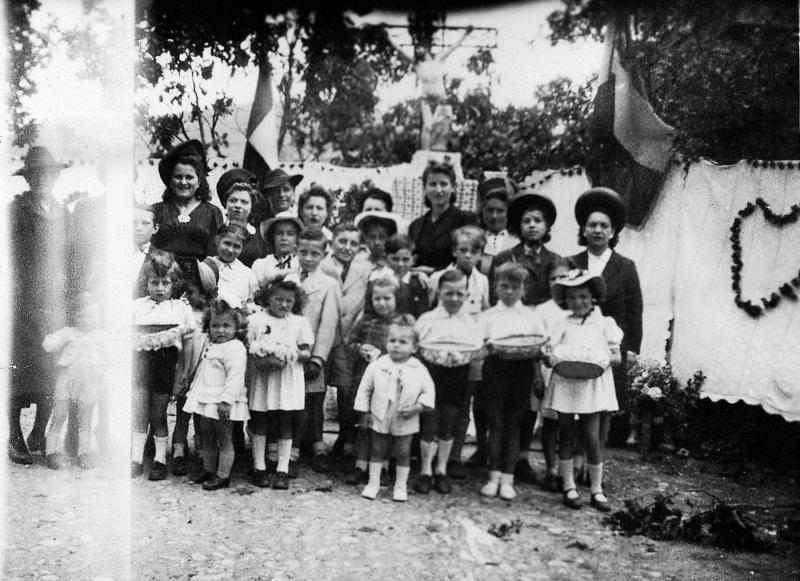 ​Paroissiennes (parroquianas) et enfants avec des petites corbeilles (desquets) devant une croix (crotz) décorée pour la Fête-Dieu, à Vendeloves, 1940-1941
