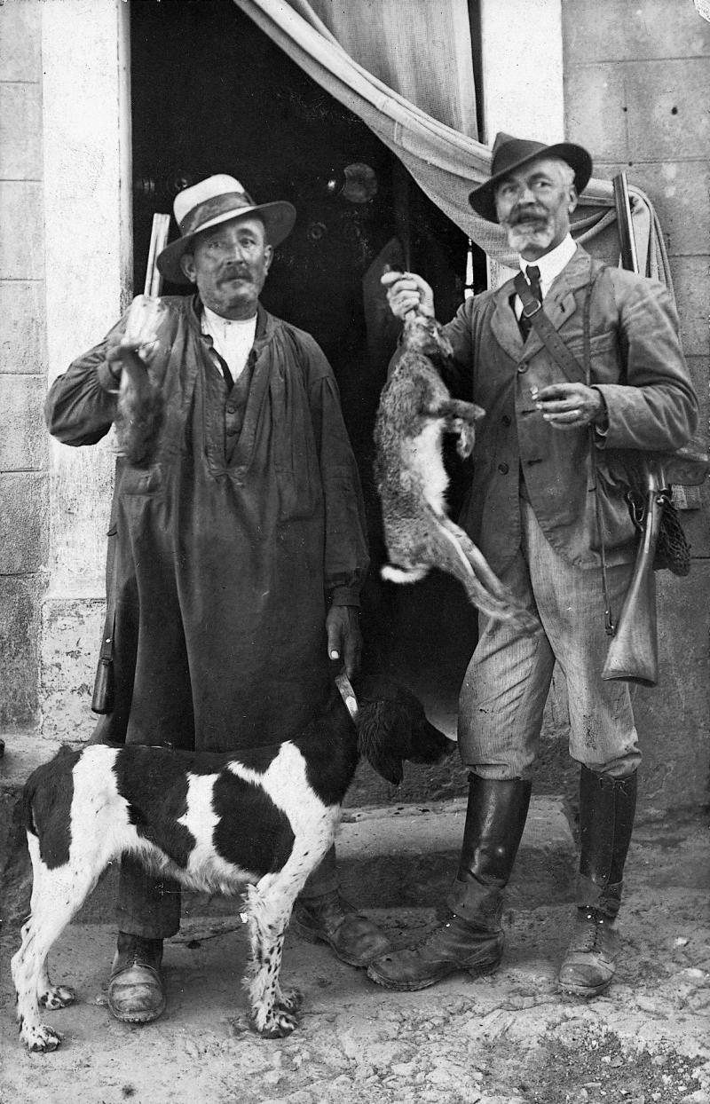​Deux chasseurs (caçaires) présentant un lièvre (lèbre) avec un chien (can), vers 1930