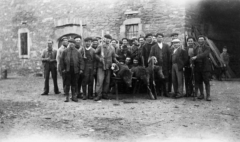 Chasseurs (caçaires) avec deux chiens (cans) et trois sangliers (pòrcs singlars, singlars) abattus devant une étable (estable), aux Estevenens, vers 1950
