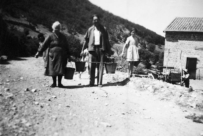 ​Femme et homme transportant des seaux (farrats) avec un cercle en bois, fillette et homme à côté d'un break, à Montclarat, 1936