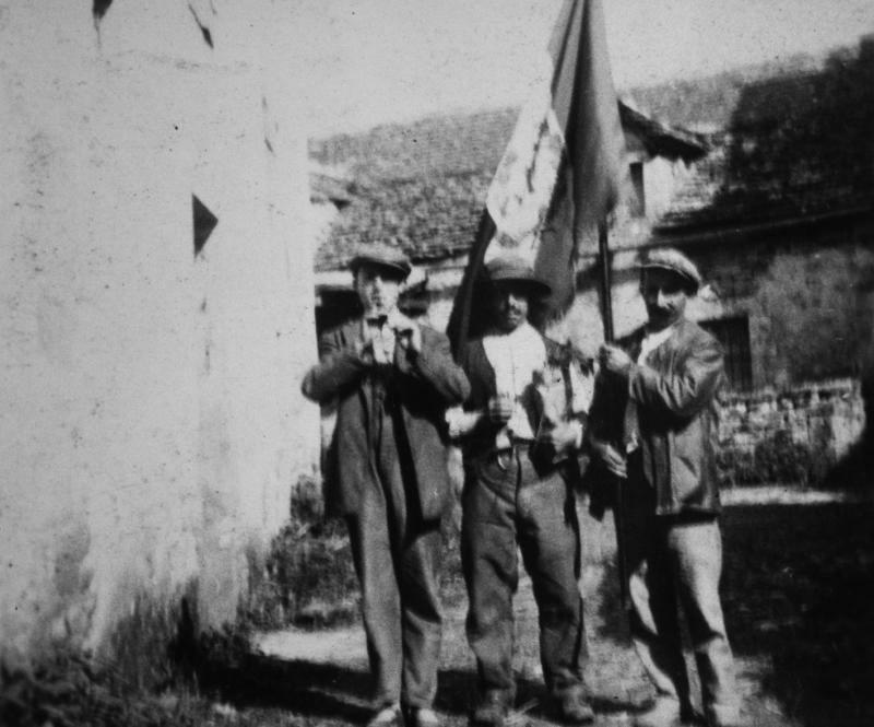 Trois conscrits avec un drapeau (drapèu) devant une maison (ostal)