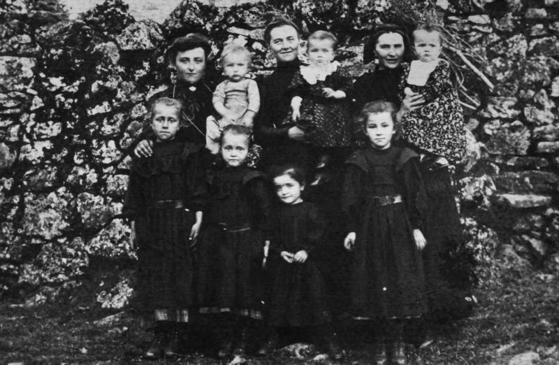 Trois femmes avec sept enfants (dròlles, enfants) devant un muret (paredon)