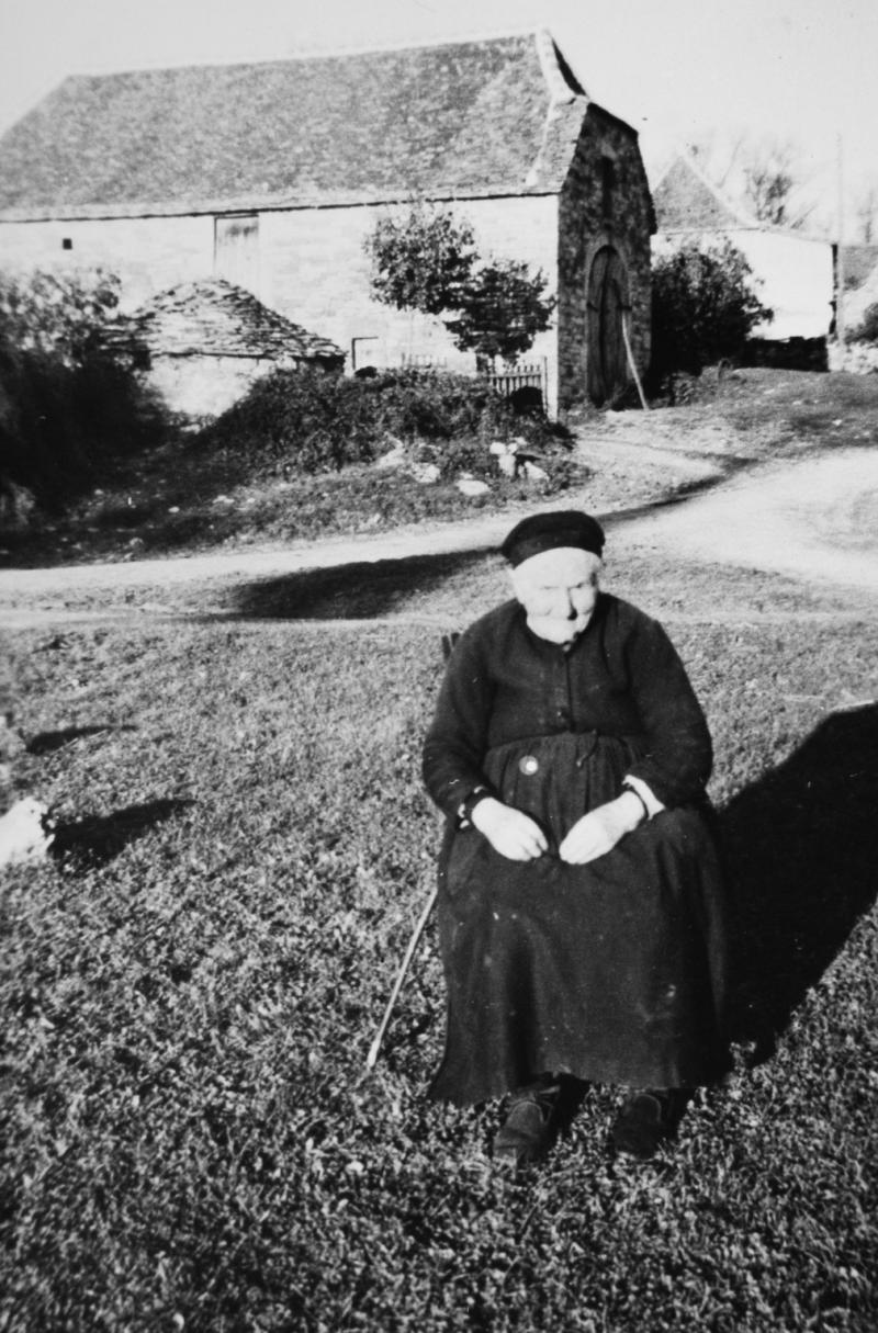 Femme assise devant un four (forn) et une grange (granja), à La Plane, 1950