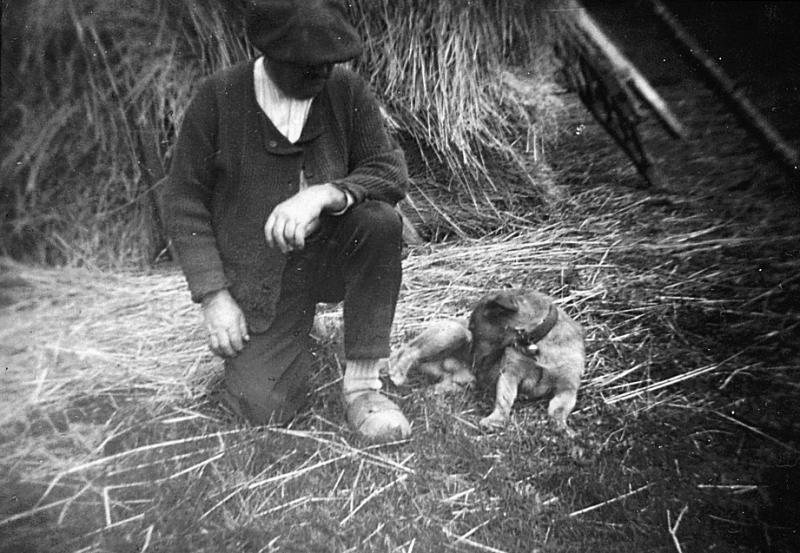 Homme accroupis et chien (can) devant une meule de paille (palhièr), à Belmont