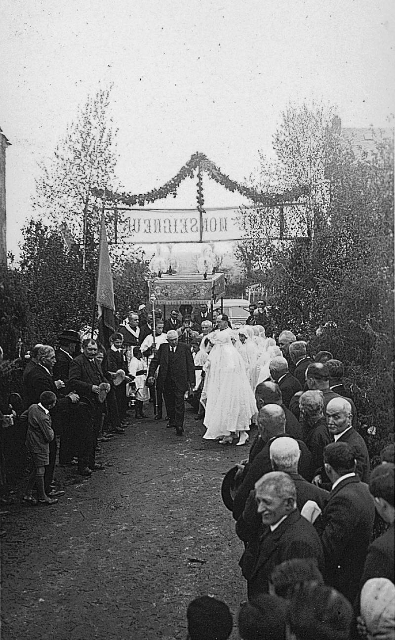 Paroissiens (parroquians) et confirmandes en aubes rassemblés autour d'un évêque (evesque) protégé par un dais pour une confirmation, mai 1938
