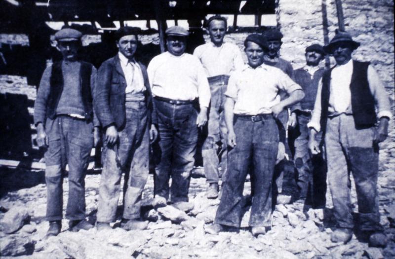 Maçons (peirièrs) et ouvriers (obrièrs) sur un tas de pierres devant une grange (fenial, granja) en construction