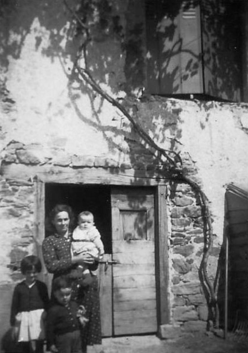 Femme et trois enfants devant une porte coupée de cave (cava), à La Tourenie, 1953