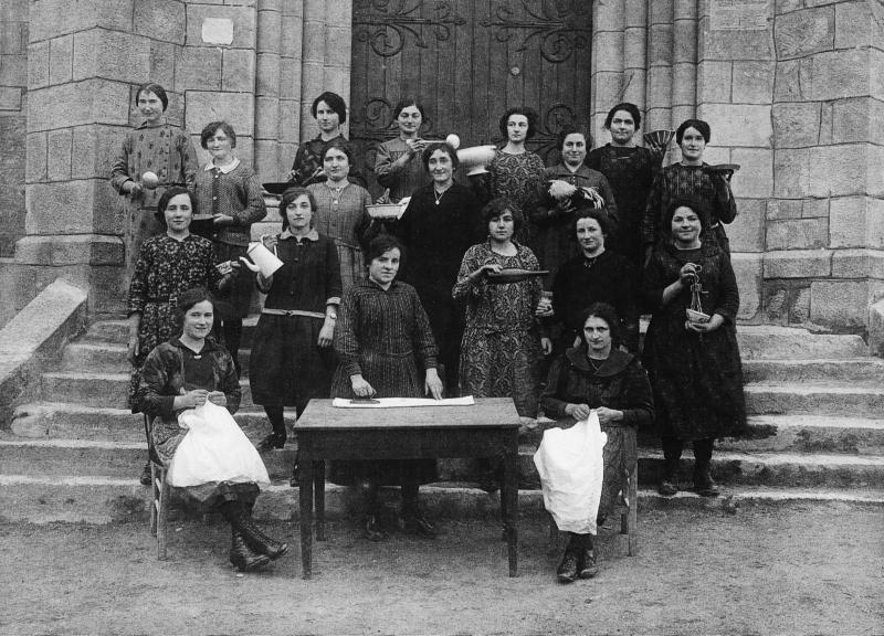 Elèves des cours ménagers avec accessoires de cuisine, de couture ou de repassage devant la porte de l'église (glèisa), janvier-février 1926