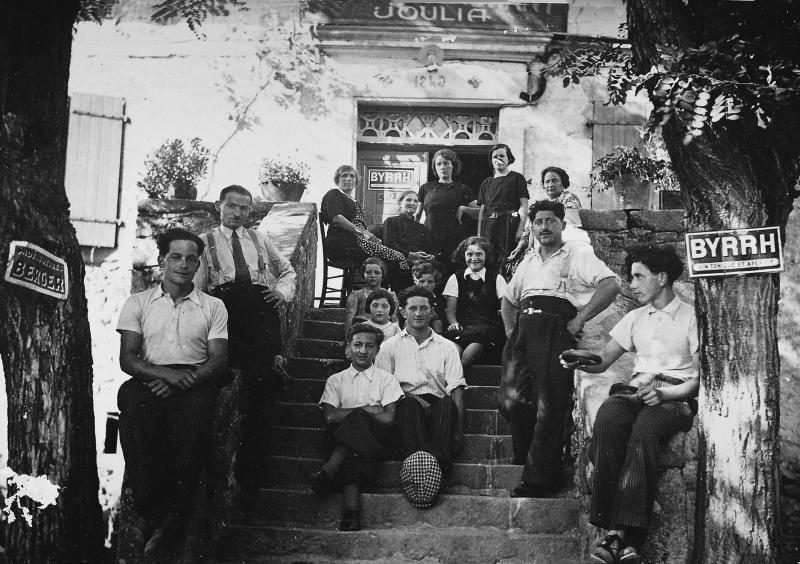 Forgeron (fabre, faure) et sa famille dans les escaliers (escalièrs) et sur le perron (pompidor) de leur auberge (aubèrja), été 1936