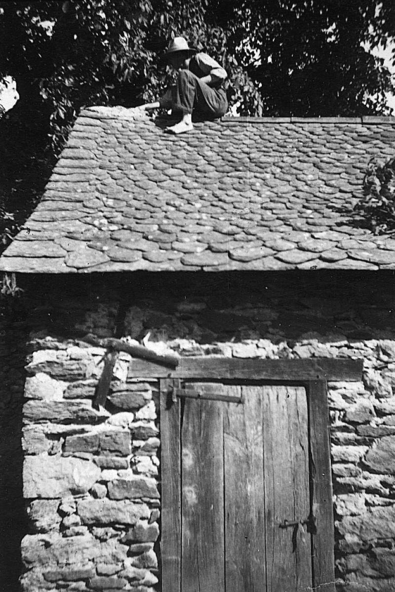 Homme sur la toiture (teulada) d'un séchoir à châtaignes (secador) effectuant des réparations au faîtage (minal), à Ayres