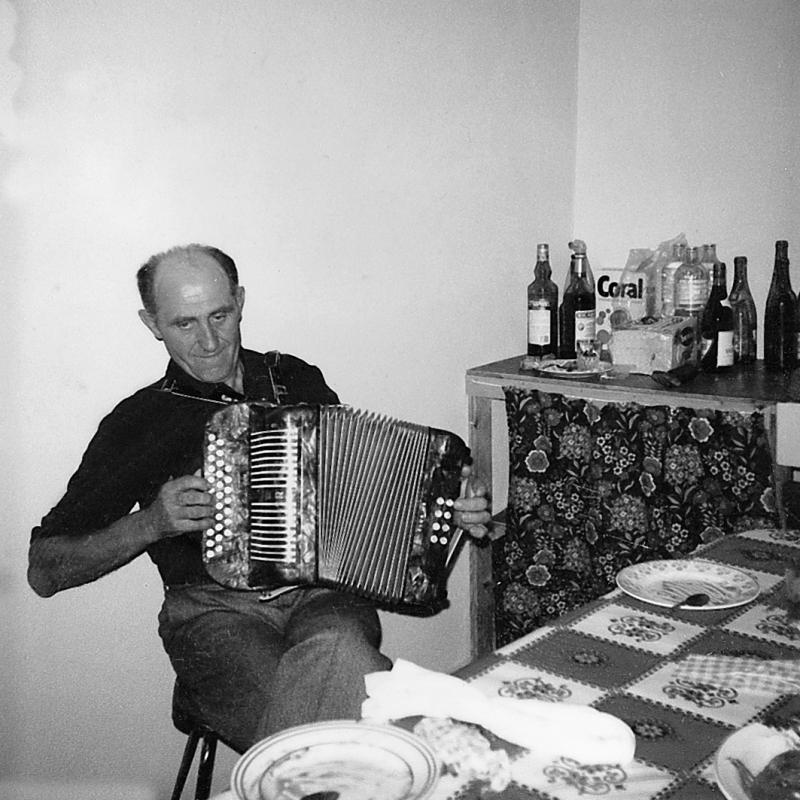 Homme assis à une table (taula) jouant de l'accordéon (acordeon) diatonique, à La Fageole