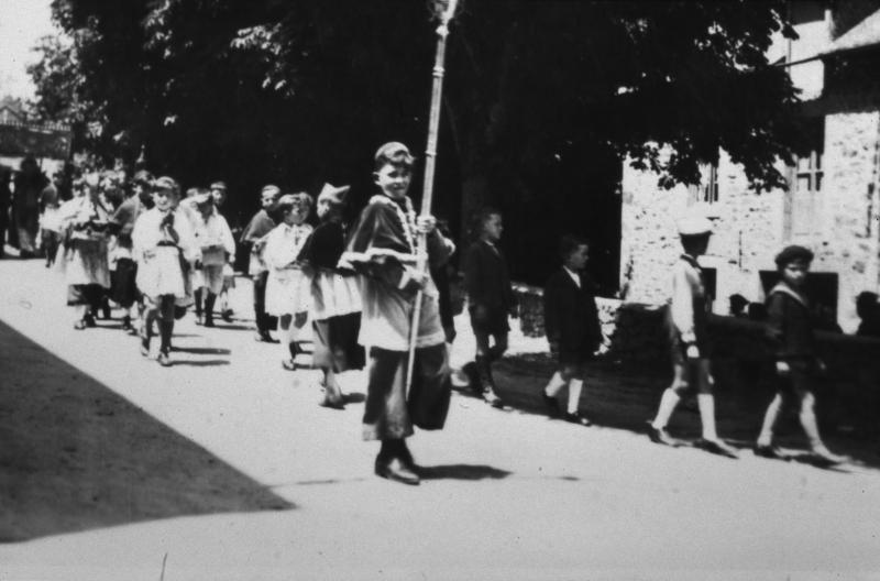 Enfants de chœur (clergues), dont un avec une croix processionnelle, et enfants (dròlles, enfants) en procession pour la Fête Dieu (Fèsta Diu), juin 1942