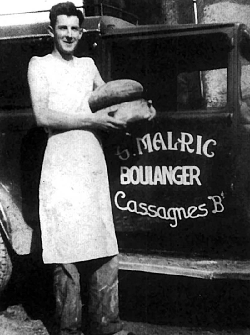 Boulanger (bolangièr) avec deux miches (michas, tortas) de pain à la main devant sa camionette de livraison, 1933